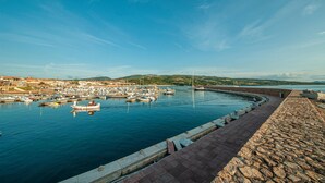A coastal marina with boats docked, a stone quay, and a hilly landscape in the background.