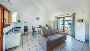 Une cuisine compacte équipée d’une cuisinière à gaz, d’une table à manger avec des chaises, d’un canapé et d’une porte-fenêtre coulissante donnant sur un balcon.