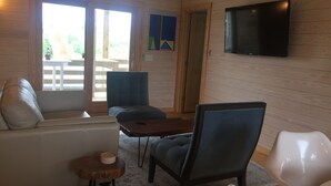 Een moderne woonkamer met een bank, stoelen, een salontafel en een flatscreen televisie aan de muur.