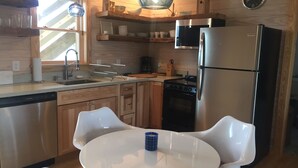 Een moderne keuken met houten kastjes, roestvrijstalen apparatuur, een ronde eettafel met stoelen en een hanglamp.