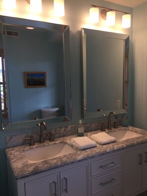 Une salle de bain avec deux lavabos, un grand miroir et un tableau accroché au mur.