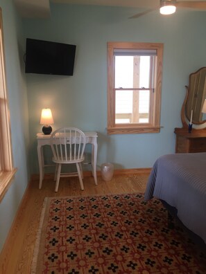 Une chambre à coucher comprenant un lit, un bureau avec une chaise, un téléviseur fixé au mur, une fenêtre et un miroir.