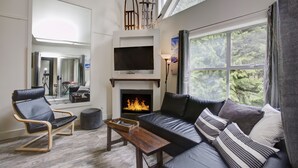Ein modernes Wohnzimmer mit Kamin, einer Couch, einem Sessel und einem Fernseher.