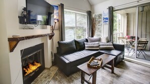 Ein modernes Wohnzimmer mit Kamin, einem großen Flachbildfernseher, einer schwarzen Ledersofa und einem Holztisch.