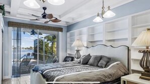 Ein Schlafzimmer mit einem Bett, Nachttischlampen, einem Deckenventilator und Blick durch eine Glastür.