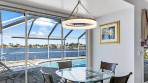 Ein modernes Zimmer mit Glastisch und -stühlen, einem großen Fenster mit Meerblick und einer Deckenleuchte.