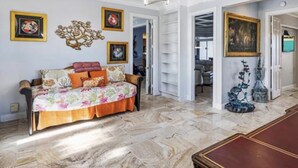 Ein geräumiges Wohnzimmer mit einer Couch, einem Couchtisch und einem Esstisch. An den Wänden befinden sich gerahmte Kunstwerke und auf dem Boden ein dekoratives Kunstobjekt.