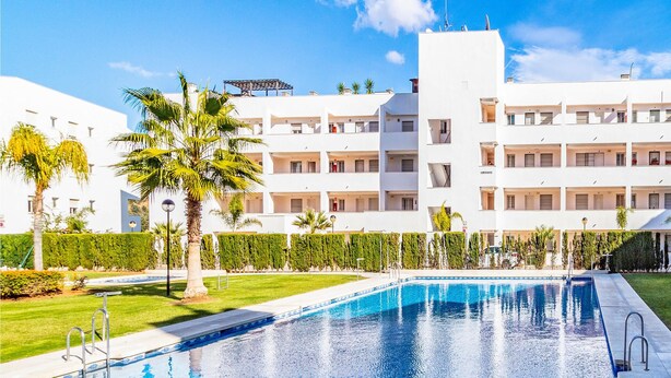 A modern hotel with a swimming pool, surrounded by well-maintained lawns and palm trees. - Nice apartment in Mijas Costa with swimming pool (Mijas Costa)