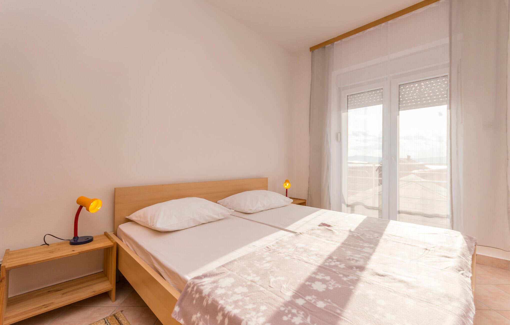 Una camera da letto con un letto in legno, due cuscini, un comodino con una lampada e vista attraverso un'ampia finestra.