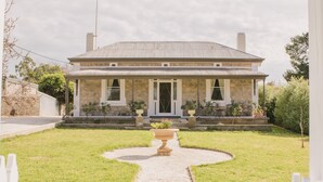 A stone house with a covered porch, a gravel pathway, and a well-maintained lawn. - Devitt on French is a quiet, romantic stone cottage in Angaston, Barossa Valley (Angaston)