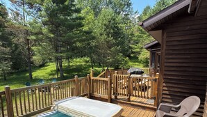 A wooden deck with a hot tub, outdoor furniture, and a view of a forested area.