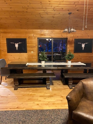 A wooden interior with a large dining table, benches, and two framed cow skulls on the walls.