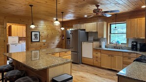 A kitchen with wooden cabinets, granite countertops, a refrigerator, a dishwasher, and a ceiling fan.