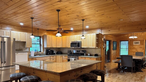 A kitchen with wooden cabinets, granite countertops, a central island with stools, and a dining area with a table and chairs.