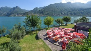 Une terrasse au bord du lac, agrémentée de parasols rouges et blancs, dotée d’un sol en pierre et offrant une vue sur le lac et les montagnes.