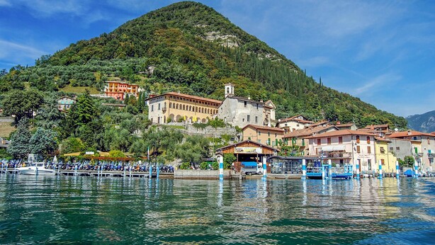 Une ville au bord d’un lac, avec des bâtiments construits sur une colline, des bateaux amarrés le long de la rive et un ciel dégagé.