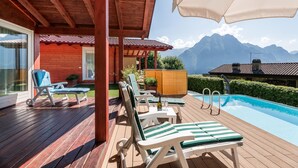 Une terrasse en bois avec une piscine, des chaises longues et une vue sur les montagnes.