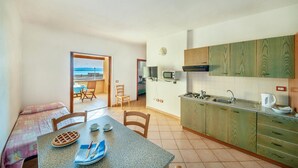 Una cocina compacta con vista al mar, un comedor con una mesa para dos personas y una pequeña sala de estar con televisor y ventana.