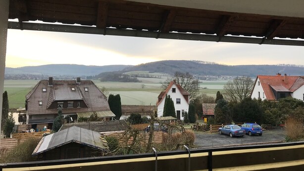 Un paysage rural avec des maisons, un espace de stationnement et une vue sur des collines lointaines.