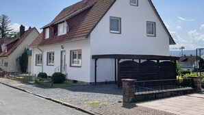 Une maison à deux étages avec un toit recouvert de tuiles rouges, un garage et un petit jardin.