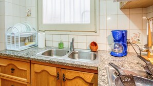 A kitchen with a double sink, dish rack, coffee maker, and wooden cabinets. - Beach front apartment in Sant Antoni de Calonge (Sant Antoni de Calonge)