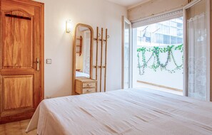 Ein Schlafzimmer mit Holztür, einem Spiegel, einem Bett mit weißer Bettdecke und einem Fenster mit Blick auf Grünfläche.