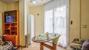 A living room with a wooden cabinet, a radiator, a table with a checkered tablecloth, and a large window with curtains. - Beach front apartment in Sant Antoni de Calonge (Sant Antoni de Calonge)