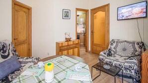 A cozy living room with a sofa, a coffee table with a checkered tablecloth, a small wooden side table, and a television mounted on the wall. - Beach front apartment in Sant Antoni de Calonge (Sant Antoni de Calonge)