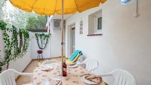 A dining area with a table set for two, white plastic chairs, a yellow umbrella, and a wall adorned with green vines. - Beach front apartment in Sant Antoni de Calonge (Sant Antoni de Calonge)