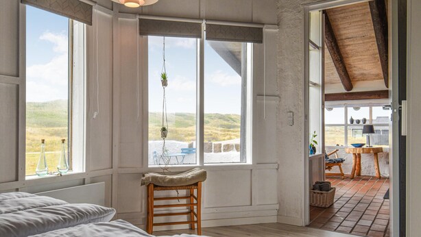 Une chambre avec une grande fenêtre, une chaise en bois et une vue sur l’extérieur.