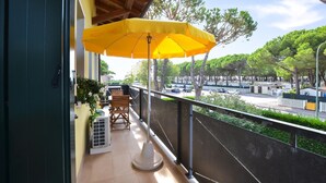 Ein Balkon mit gelber Sonnenschirm, Holzstühlen und einem Blumentopf.