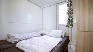 A single bed with white bedding, a window with a leaf-patterned curtain, and a wooden wardrobe. - Amazing ship in Biddinghuizen with house sea view (Biddinghuizen)