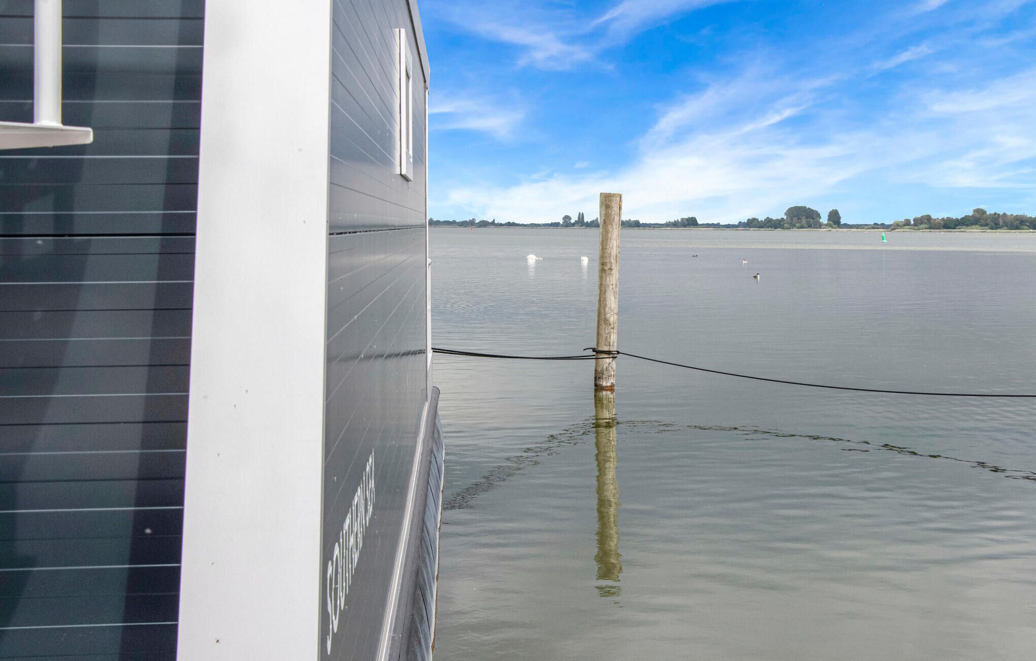 Une propriété située au bord de l’eau, avec un poteau en bois planté dans l’eau, une jetée et une vue dégagée sur l’eau et les arbres au loin.