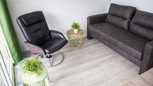 A modern living room with a black leather chair, a grey sofa, and a small round table with a plant. - Amazing ship in Biddinghuizen with house sea view (Biddinghuizen)