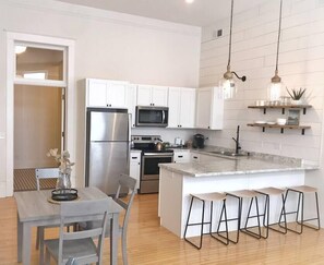 A modern kitchen with white cabinets, stainless steel appliances, a marble island, and bar stools. - Loft on Lincoln Hancock #204 (Hancock)