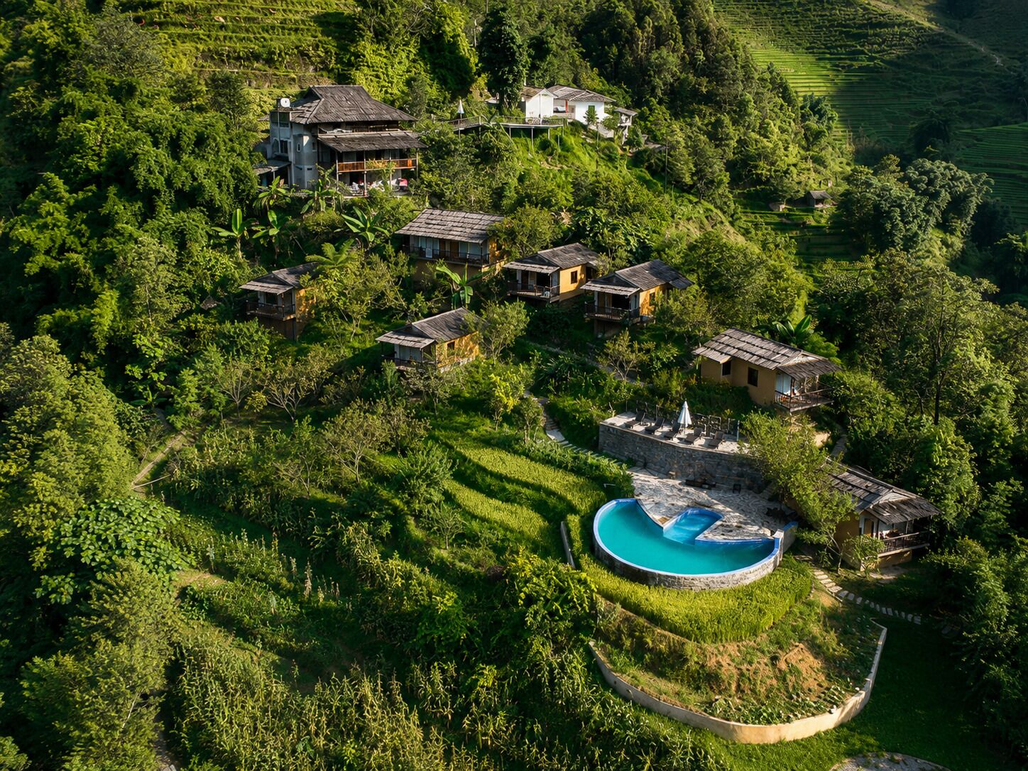Vista aérea de una propiedad en una ladera con varias edificaciones, una piscina y abundante vegetación.