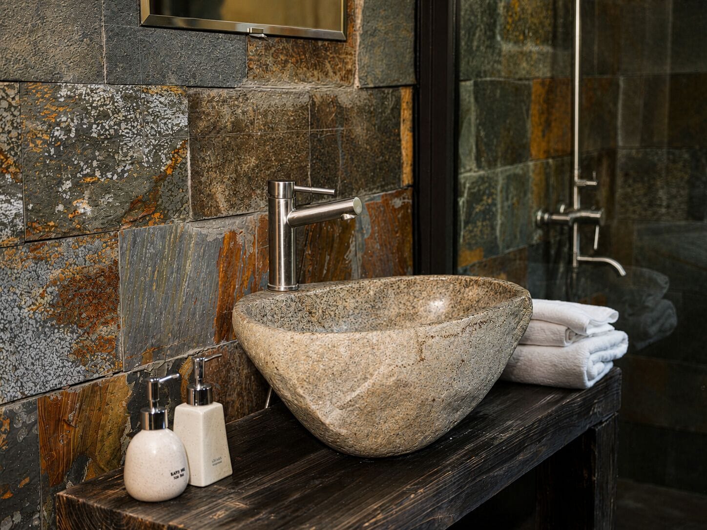 A bathroom with a stone sink, a mirror, and two bottles of soap.