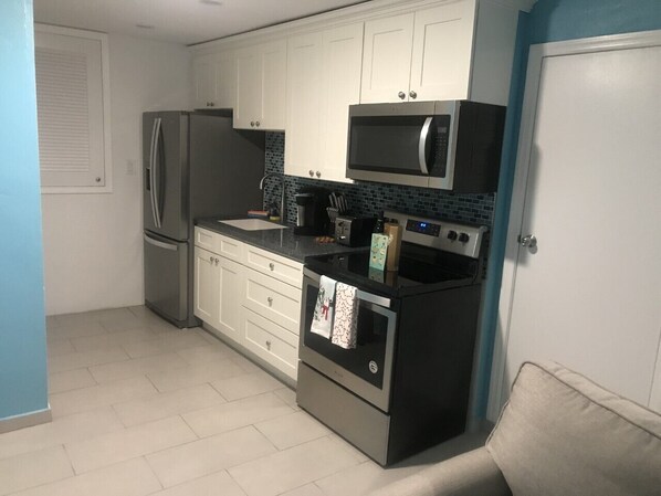A kitchen with white cabinets, a stainless steel refrigerator, a microwave, an oven, and a coffee maker.