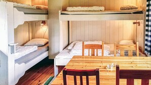 Een slaapkamer met stapelbed, een houten tafel en stoelen, een kleedje en een wandlamp.
