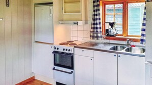 Een kleine keuken met witte kastjes, een fornuis, een spoelbak en een raam met een geruit gordijn.