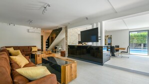 A modern living room with a brown leather sofa, wooden coffee table, and a TV mounted on a stone wall. - Lovely home in Fazana with sauna (Fazana)