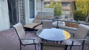 Eine Terrasse mit Gartenmöbeln, darunter ein Glastisch und Stühle, und eine Schiebeglastür, die auf einen Balkon führt.