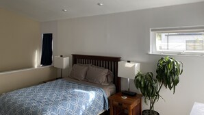 Ein Schlafzimmer mit einem Bett, zwei Nachttischlampen, einem Nachttisch, einer Topfpflanze und einem Fenster.