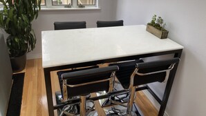Ein Essbereich mit einem weißen Tisch und vier schwarzen Stühlen mit Chrombeinen. Links steht ein Blumentopf und auf dem Tisch eine kleine Pflanze.