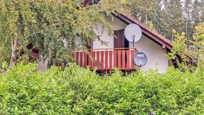 A house with a red balcony, surrounded by lush greenery.