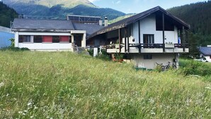 A two-story chalet with a balcony, surrounded by a grassy field and mountains in the background. - Fifinhaus 1. OG Süd by Interhome (Fiesch)
