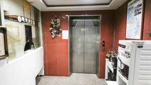 An elevator in a building with a red-tiled wall, a reception desk with a sign, and a bulletin board with a map. - Whitehouse Motel (Seosan)