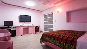 Un dormitorio con decoración rosa que incluye una cama, un escritorio, una silla, un televisor y una ventana.