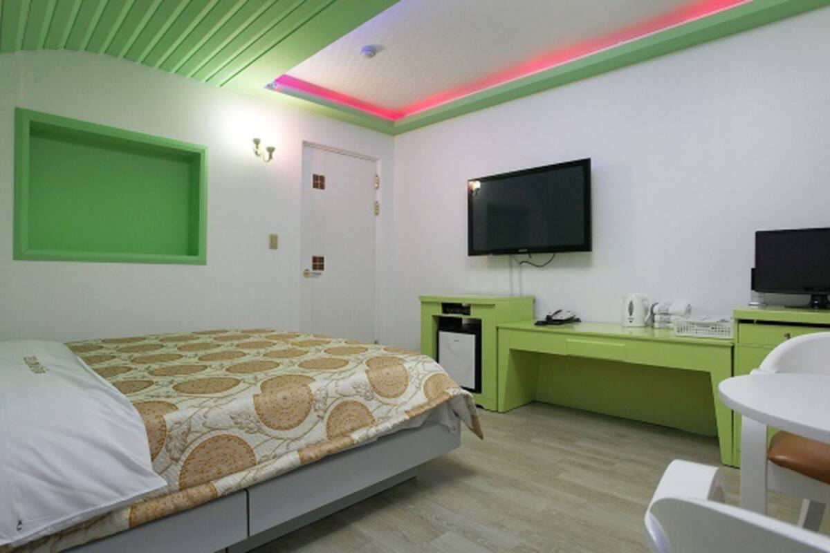 A hotel room with a bed, a desk, a chair, a TV, and a small kitchenette.