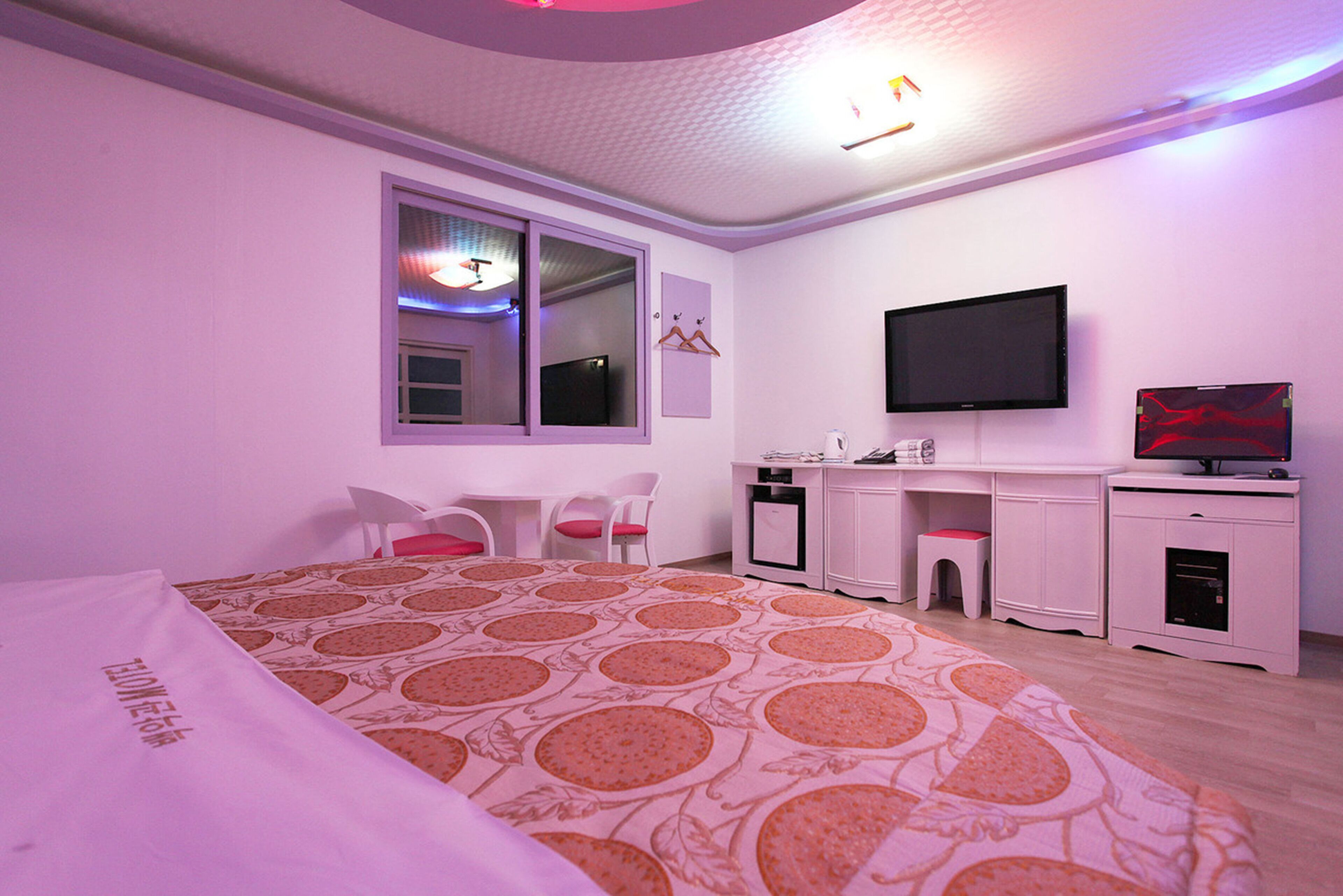 Ein Schlafzimmer mit Bett, Schreibtisch, Stuhl, Fernseher und Fenster.